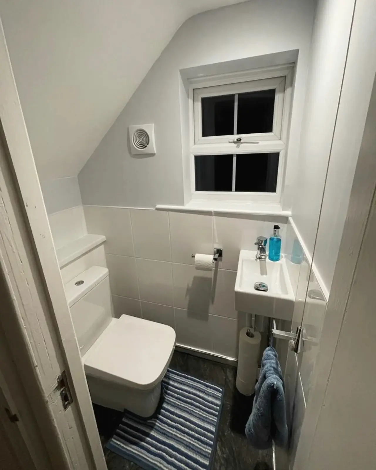 The same cloakroom after renovation, with white tiling, a new toilet and basin
