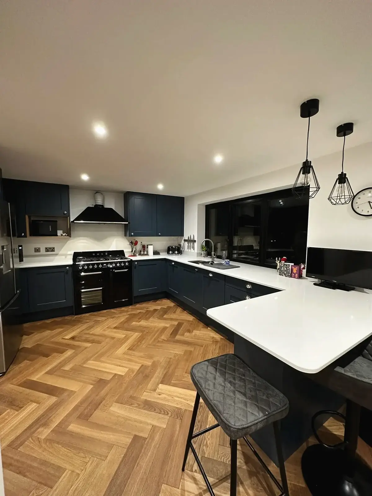 Renovated kitchen with navy units, a breakfast bar and herringbone flooring