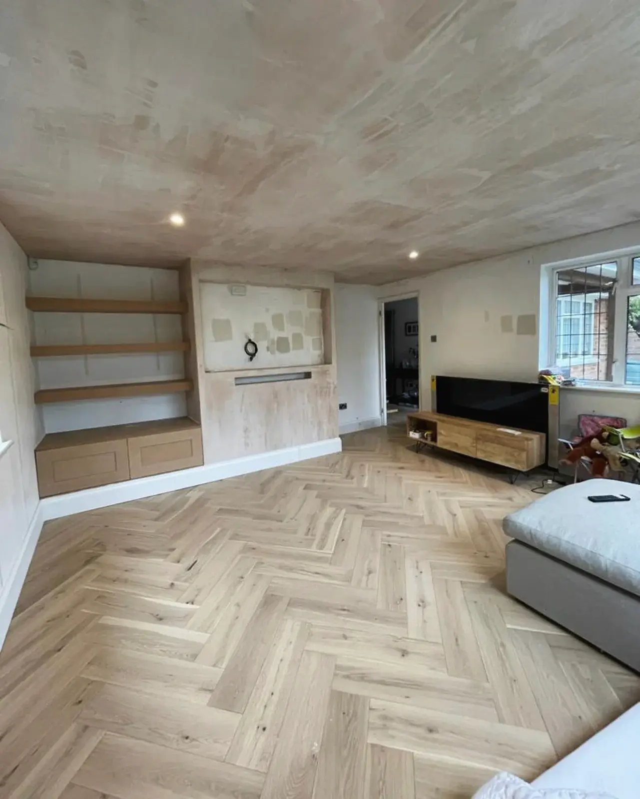 Living room after renovation, with herringbone flooring and built-in shelving