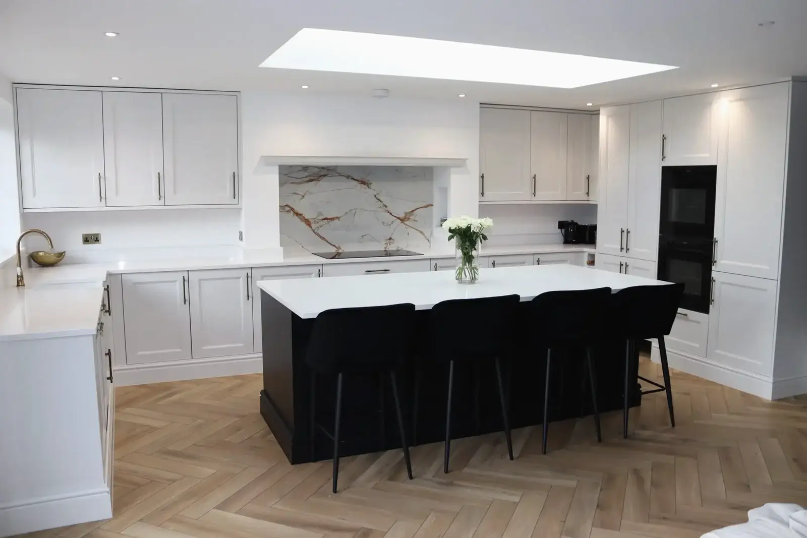 Open-plan kitchen renovation with white shaker units, a dark island, herringbone flooring and a skylight